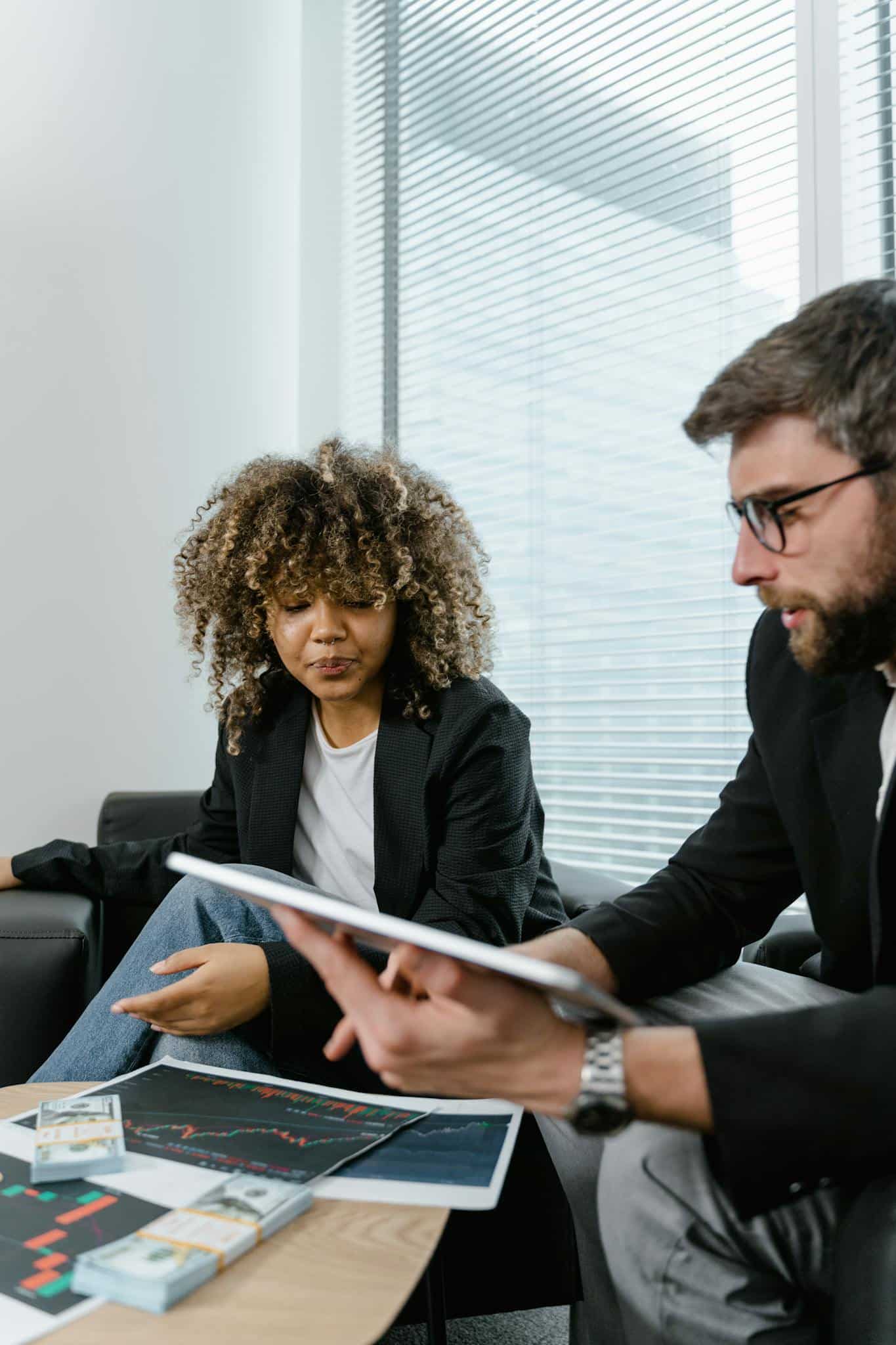 Two professionals discussing financial graphs on a tablet in a modern office setting.